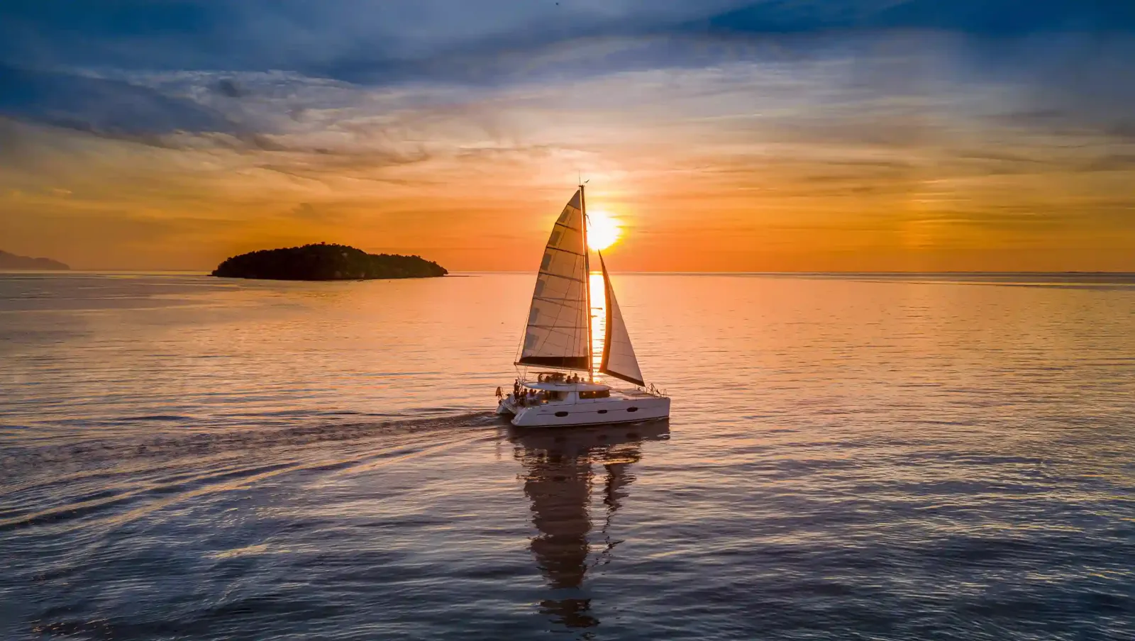 A sailing catamaran under full sail at sunset