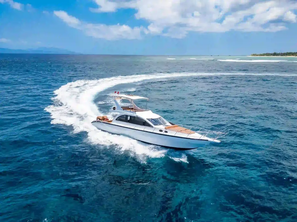 Aerial view of a white sport yacht turning at speed on open blue water