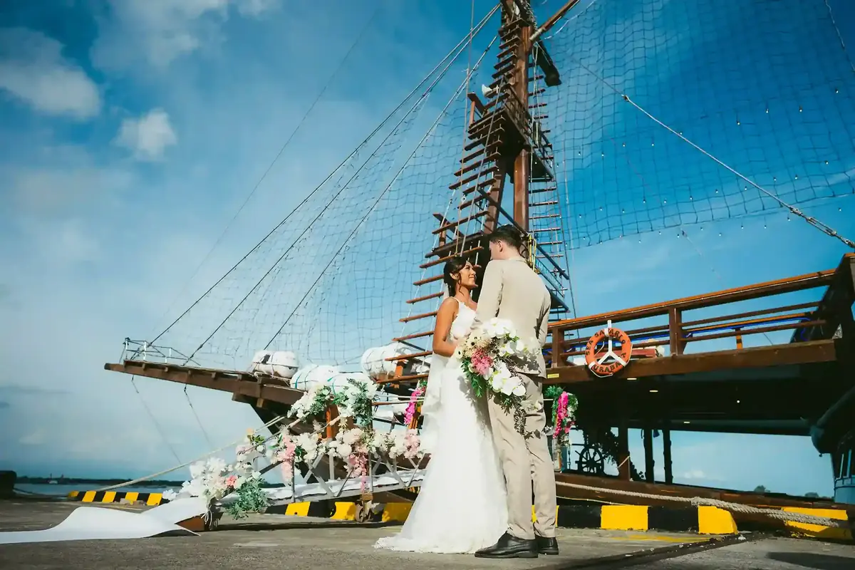 A bride and groom beneath the rigging of a tall ship at a pier