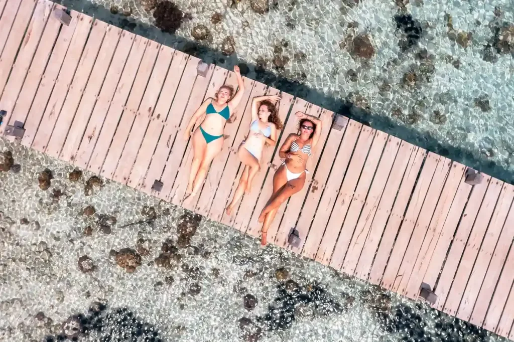 Three guests lying on a wooden jetty over clear water at Kanawa Island